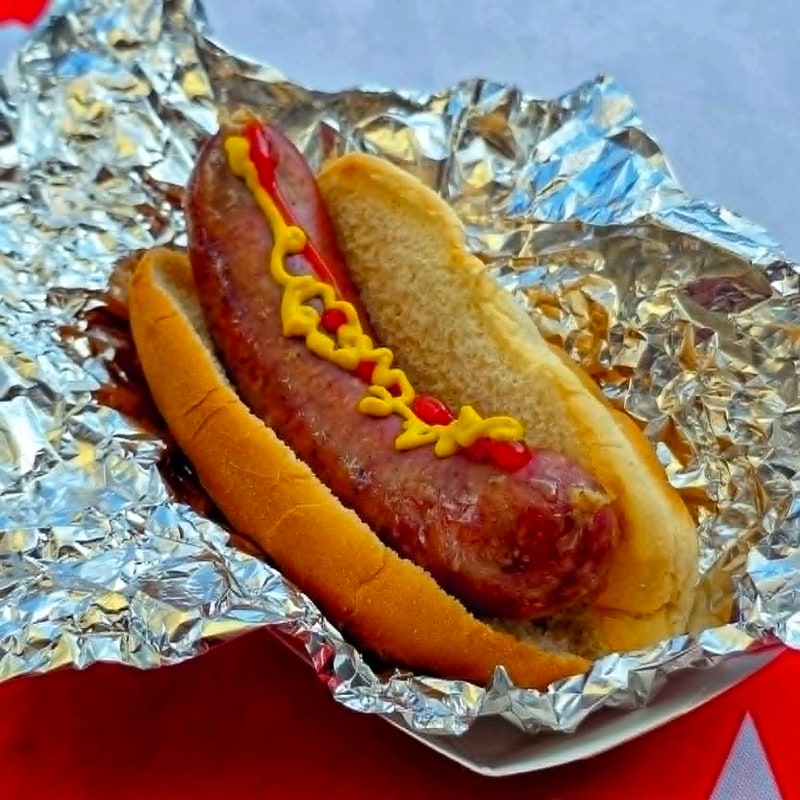 Classic brat in a bun with a mustard drizzle, wrapped in foil