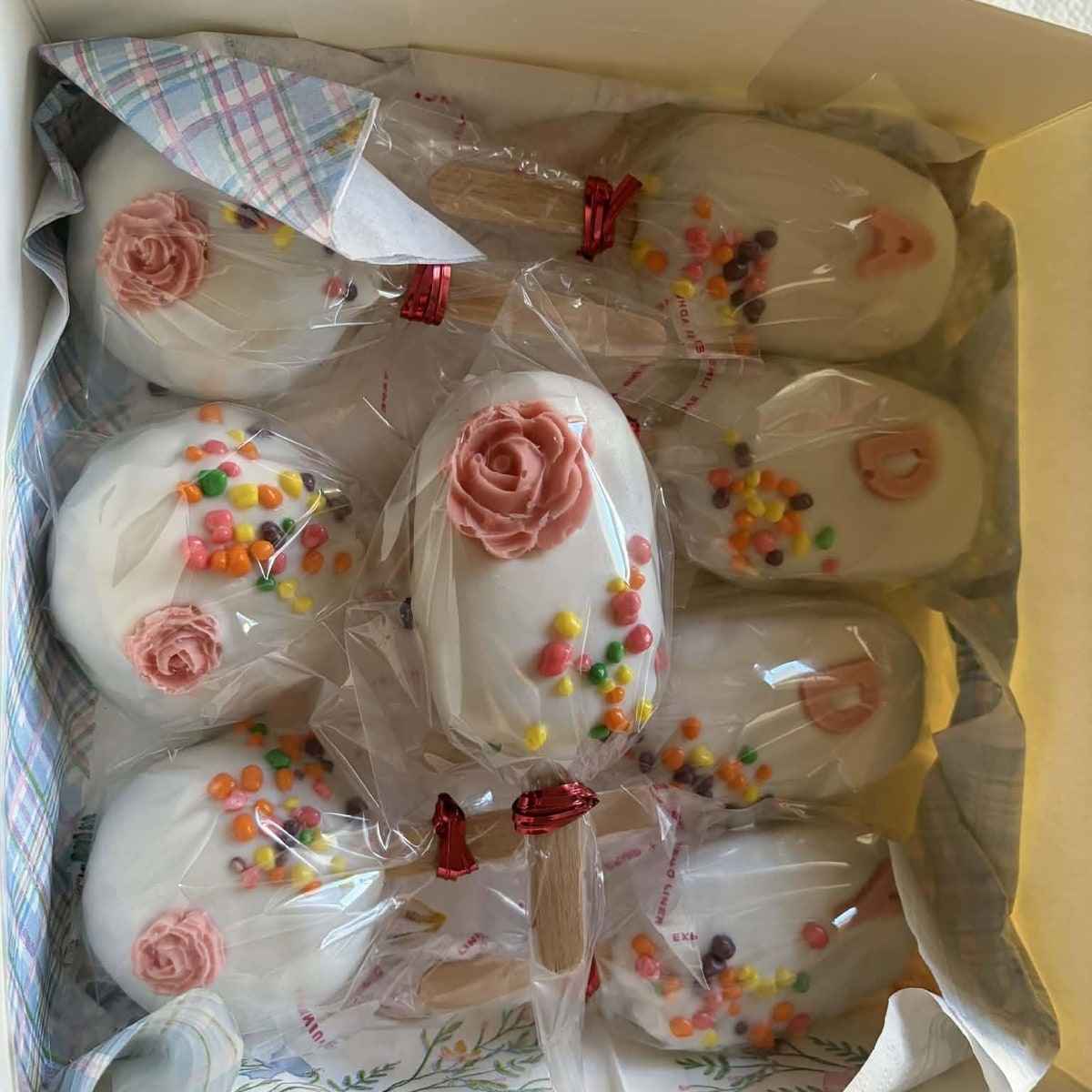 Gift box of white chocolate cakesicles decorated with pink frosting roses